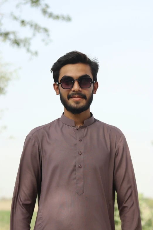 a man in a brown shirt and sunglasses is smiling for the camera