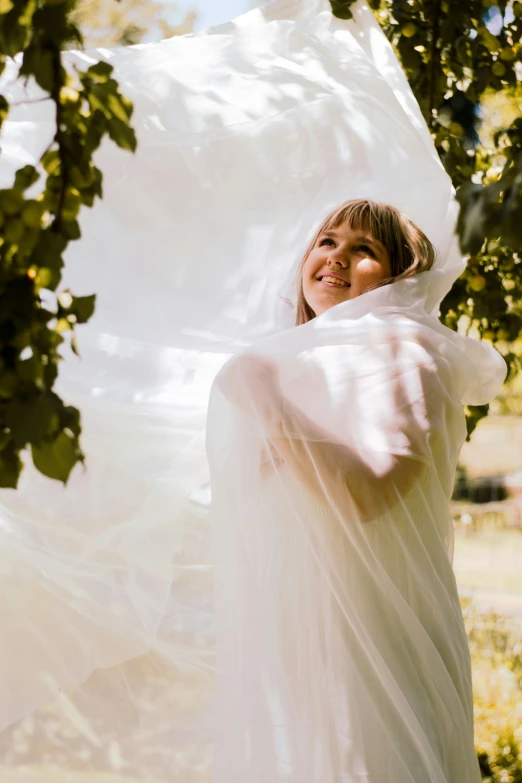 a woman in white gown hiding behind a piece of sheer fabric