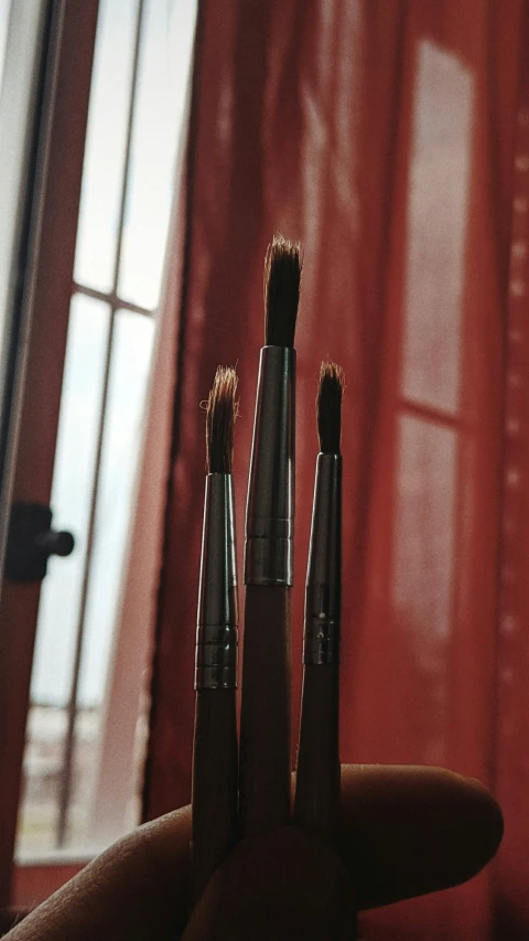three makeup brushes are shown held in front of red curtains