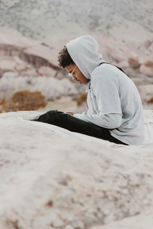 a man is sitting on the edge of a mountain looking at his phone