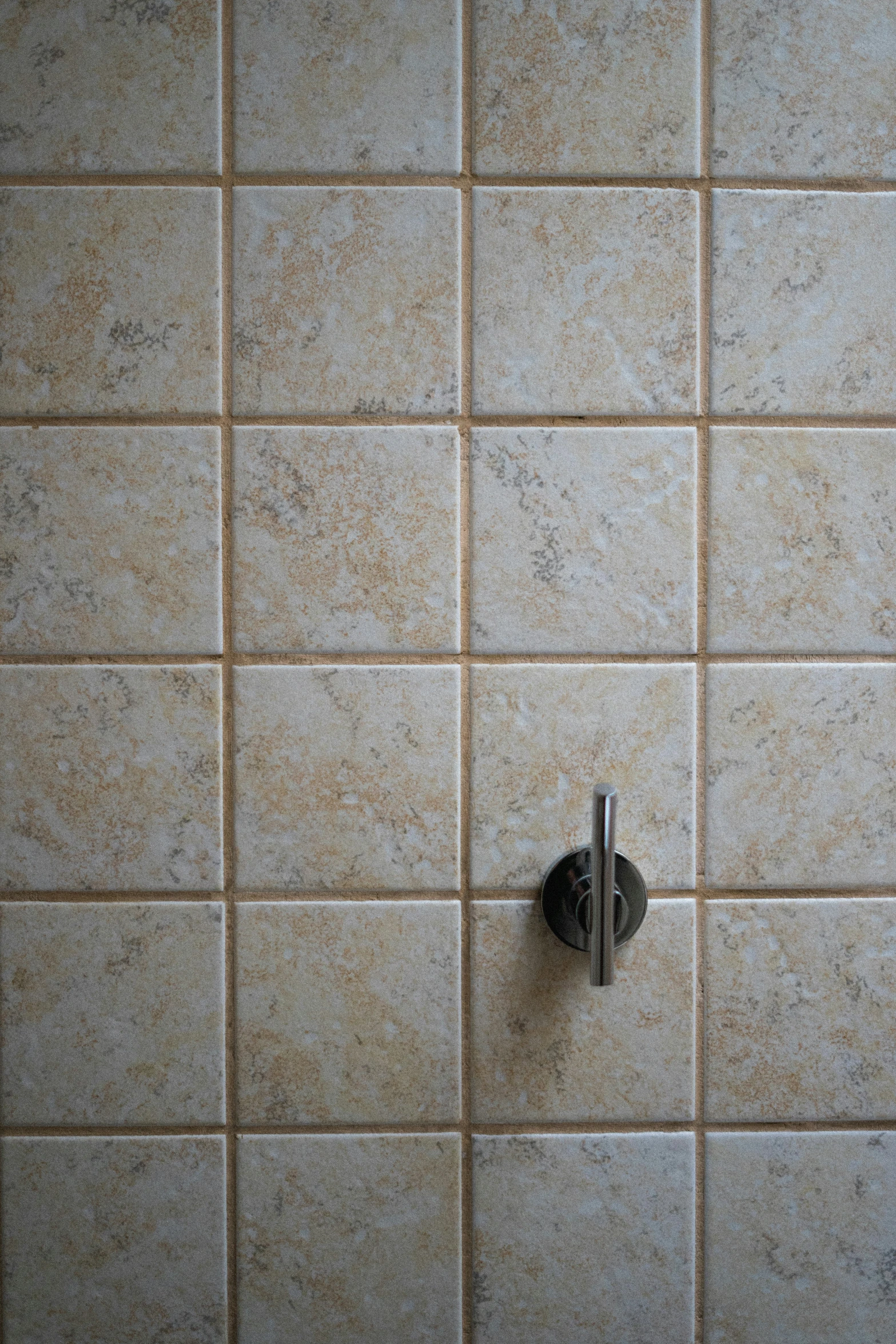 a brown tile wall and a gray metal hook