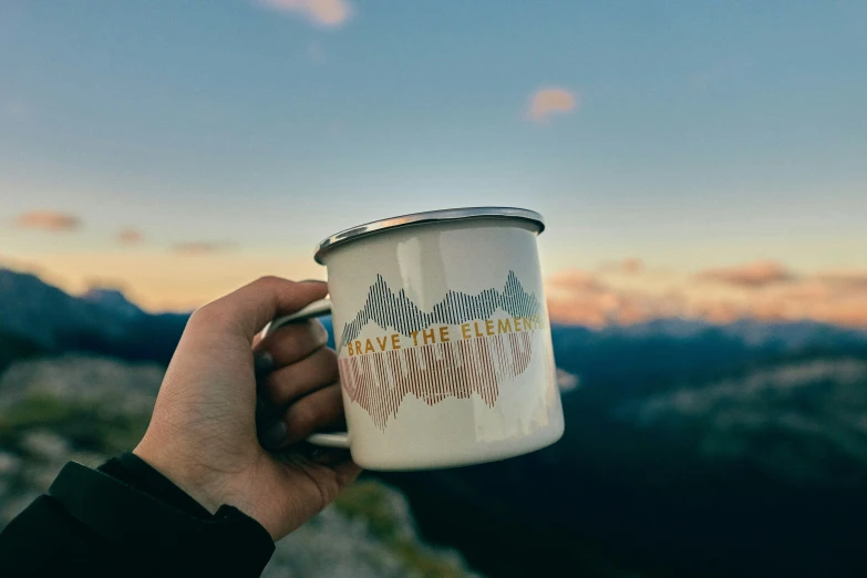 a cup of coffee held up against a mountain with mountains in the background