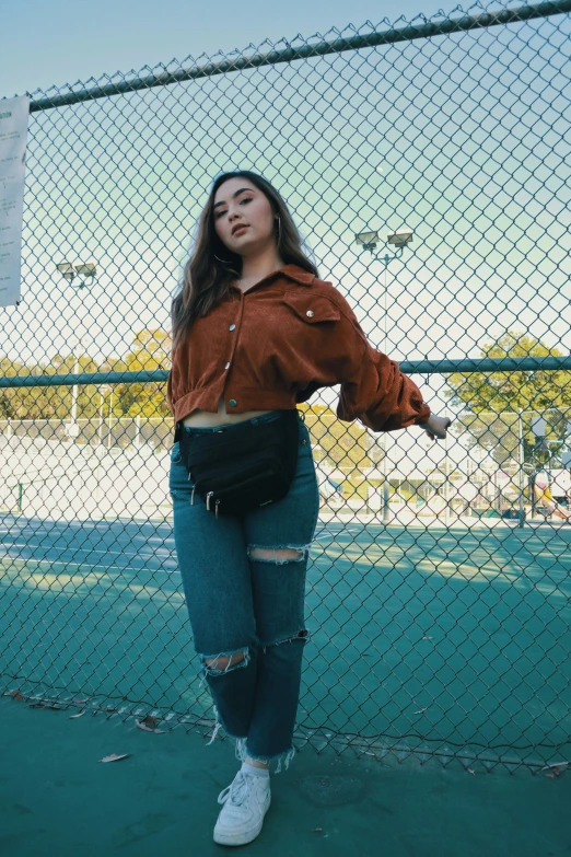 a young woman leaning against a fence with a tennis racket in her hand