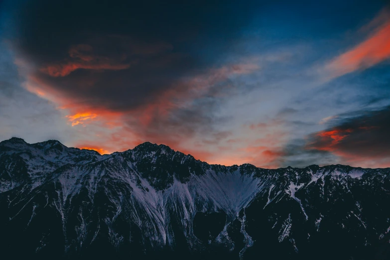 a snowy mountain range with red and blue clouds