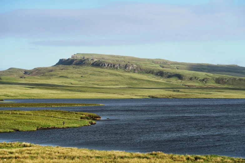 a lake in the middle of the grass with mountains behind it