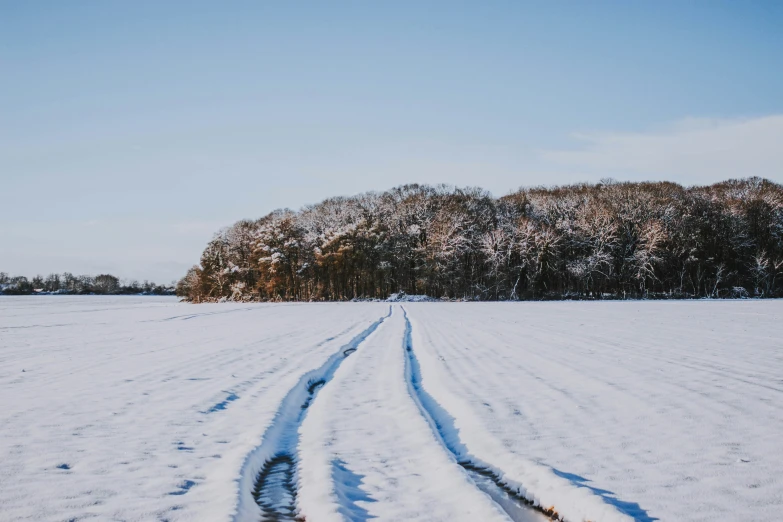 a long, thin road in front of a field with snow