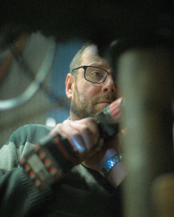 a bearded man with glasses holding a remote