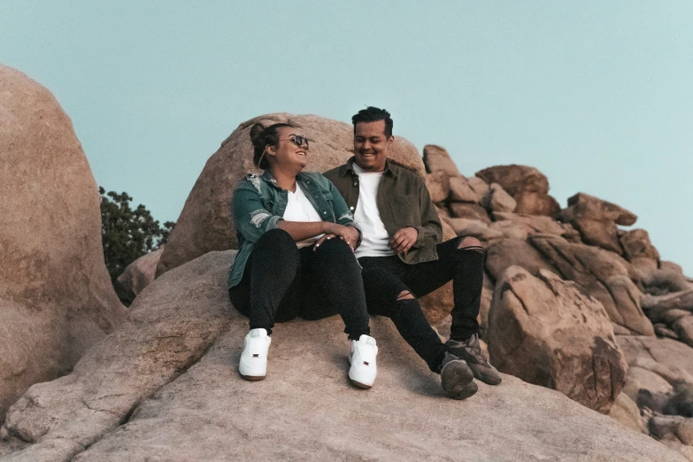 two people sit on top of a large rock