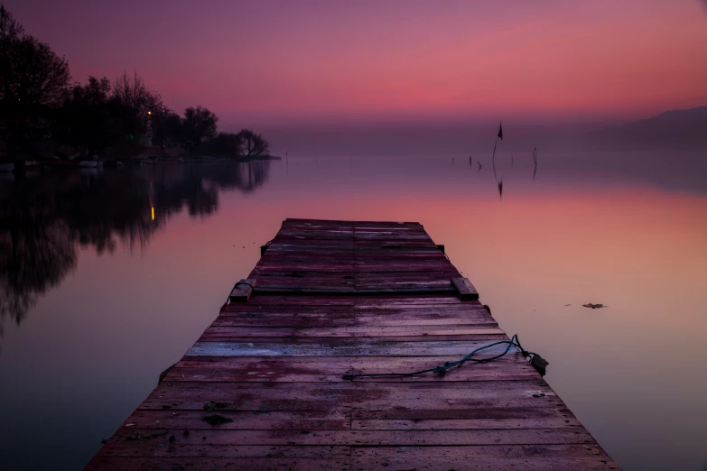 a dock next to a lake during a pink sunset