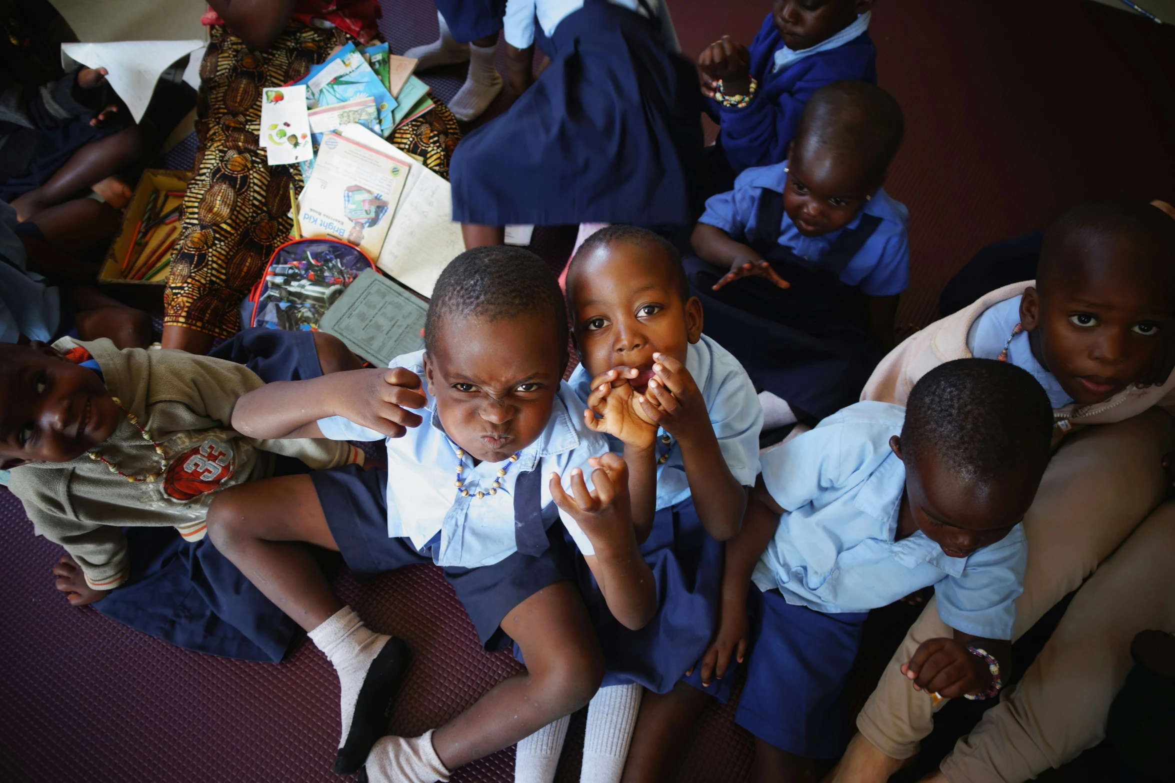 two girls and one boy sit in front of a group of other school children