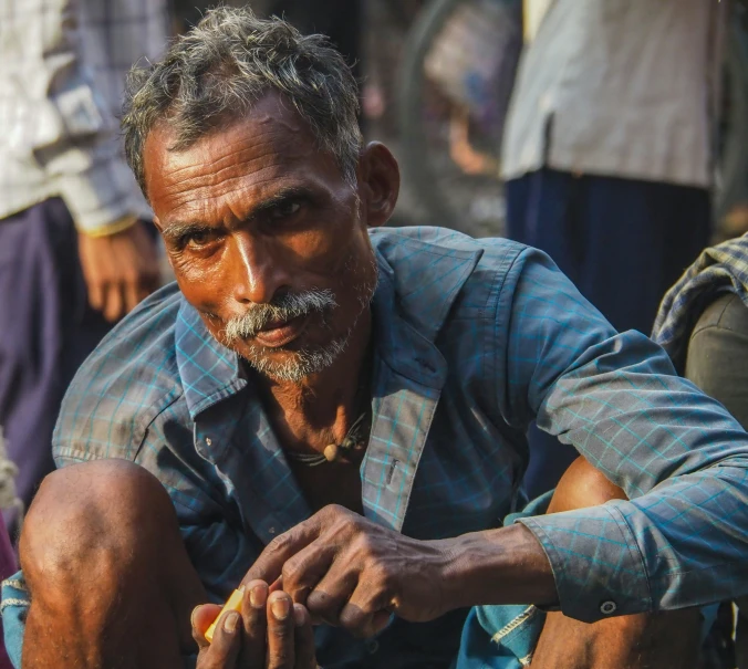 man sitting down holding food items while others gather around