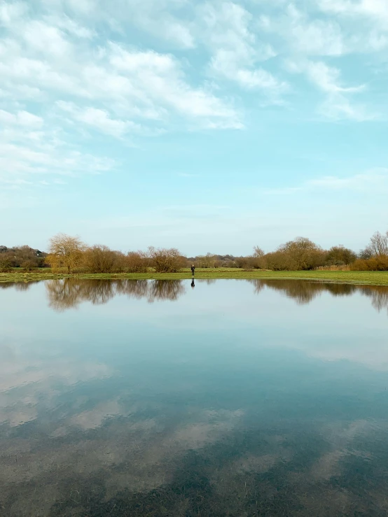 a person walking along a river near a lush green field