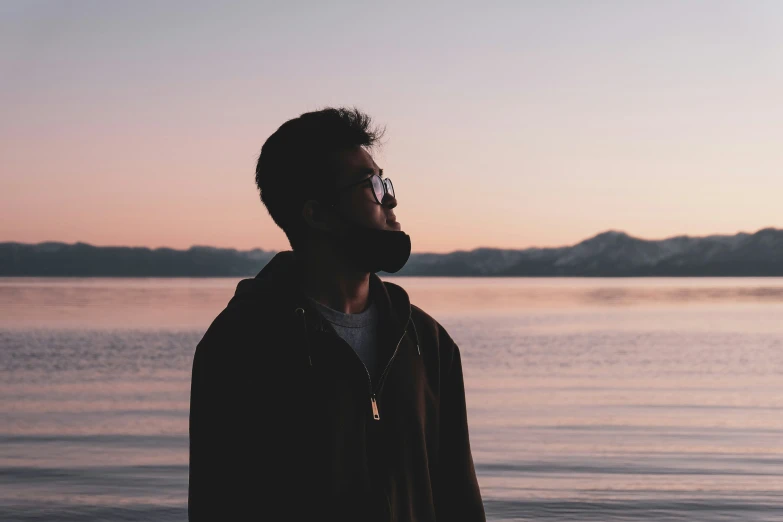 a man wearing glasses and a dark jacket standing in front of the ocean