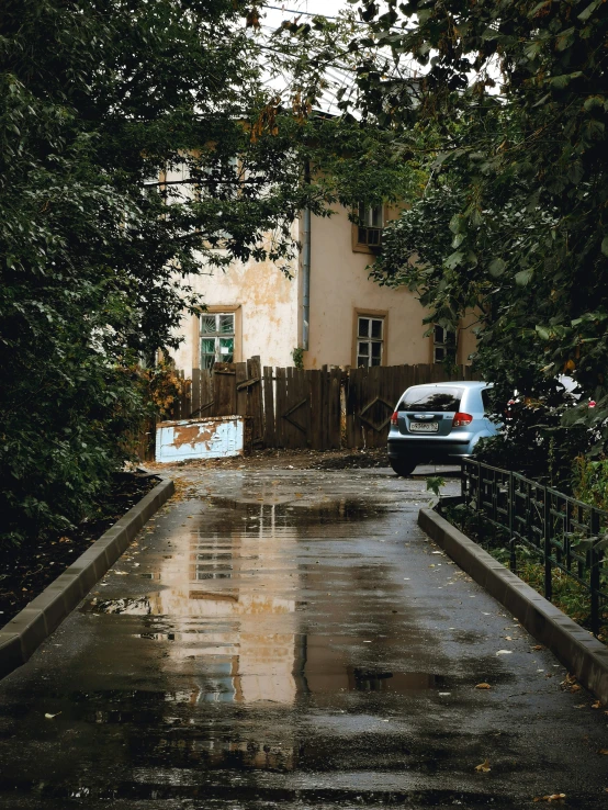 a rainy road with a white building and blue car