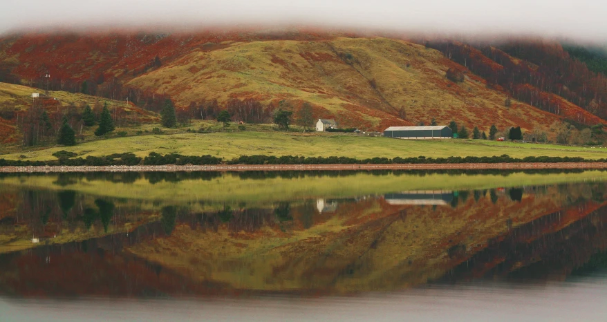 a barn that is sitting on the side of a hill next to a body of water