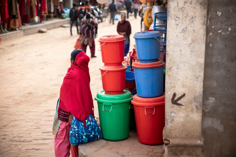 a woman stands by a stack of blue and red buckets