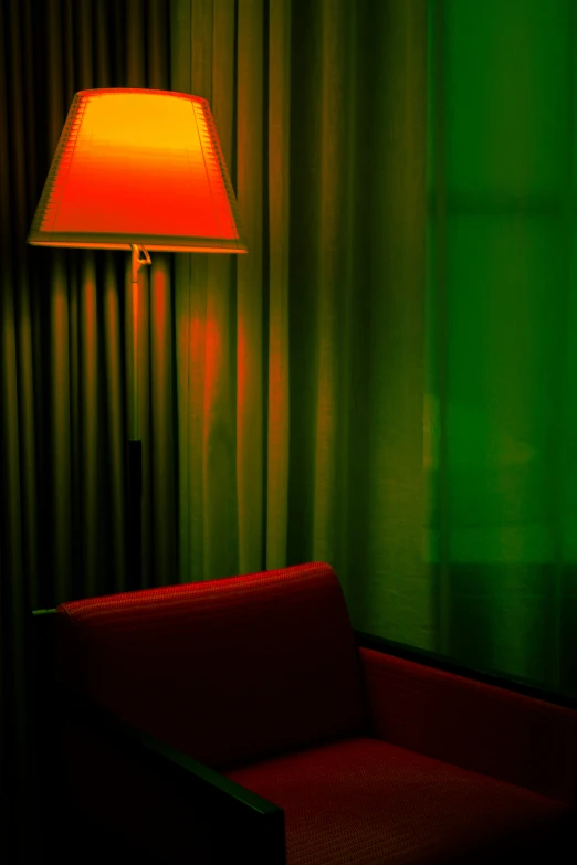 a red chair and lamp in front of green curtain