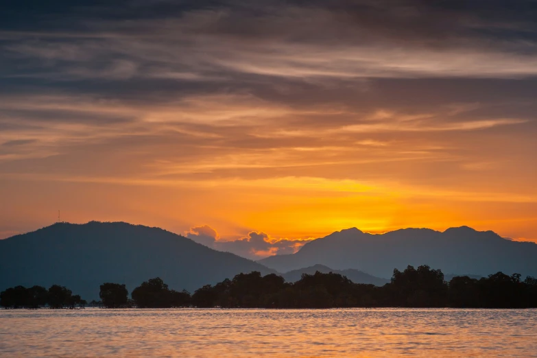 a sunrise over mountains with the clouds moving in a different direction