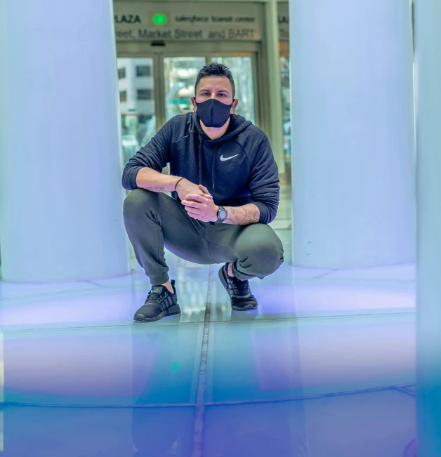 a man in a protective face mask crouches down against columns