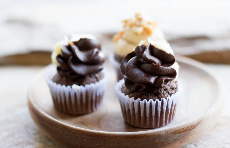 three chocolate cupcakes on a plate next to one another