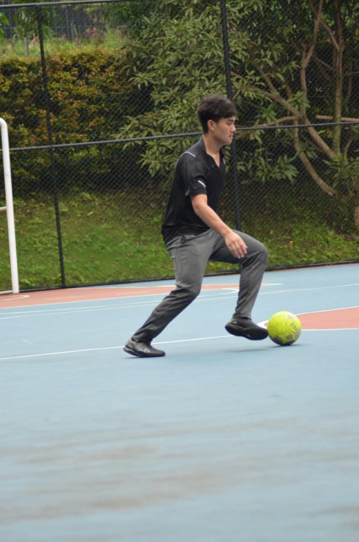 a boy playing with a tennis ball on an asphalt court