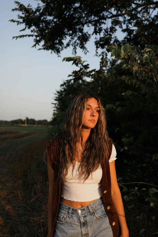 a young woman standing in a field near trees