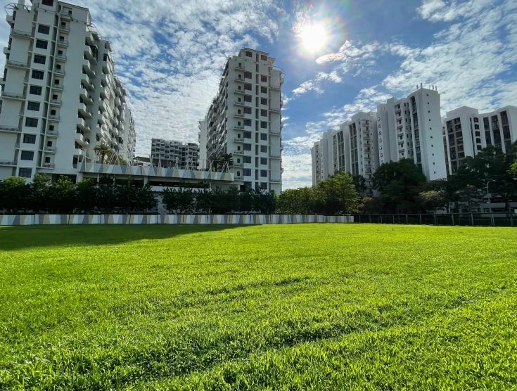 a green grassy field near many buildings under a blue sky