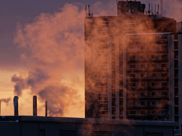 a tall brown building sitting next to smoke coming from the stacks