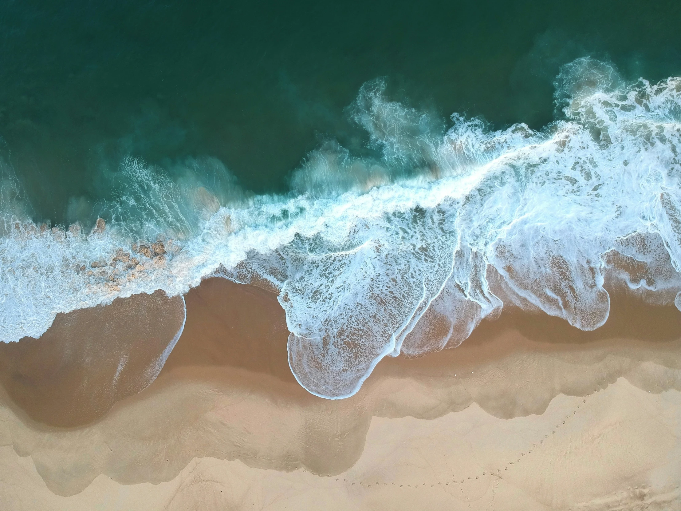 an aerial view of waves and sand at the shore