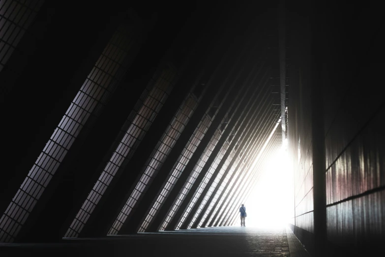a silhouette of a person walking towards the camera on a darkened walkway