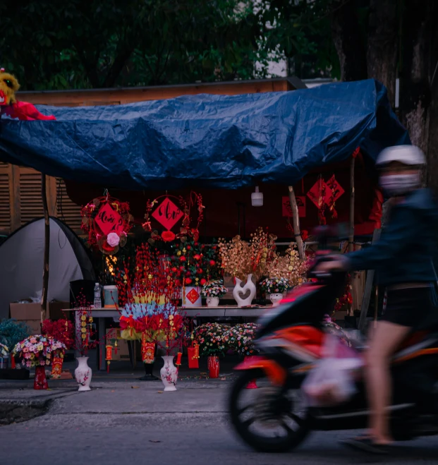 motorcycle passing near small outdoor market where large decorations are also set up