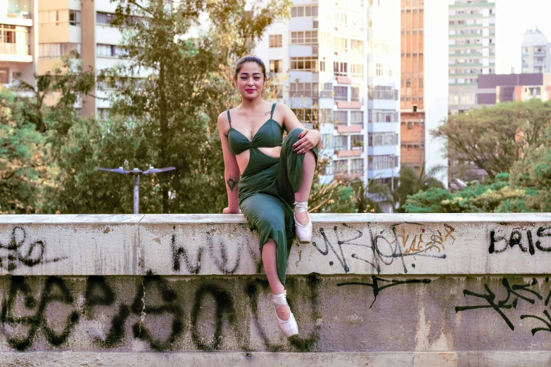 woman in green bikini top leaning on a cement wall with graffiti writing on it