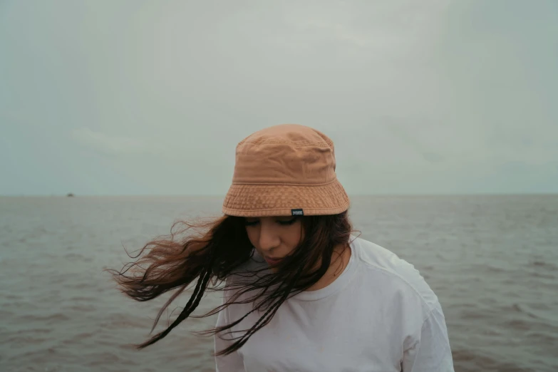 a young woman wearing a hat standing near the ocean