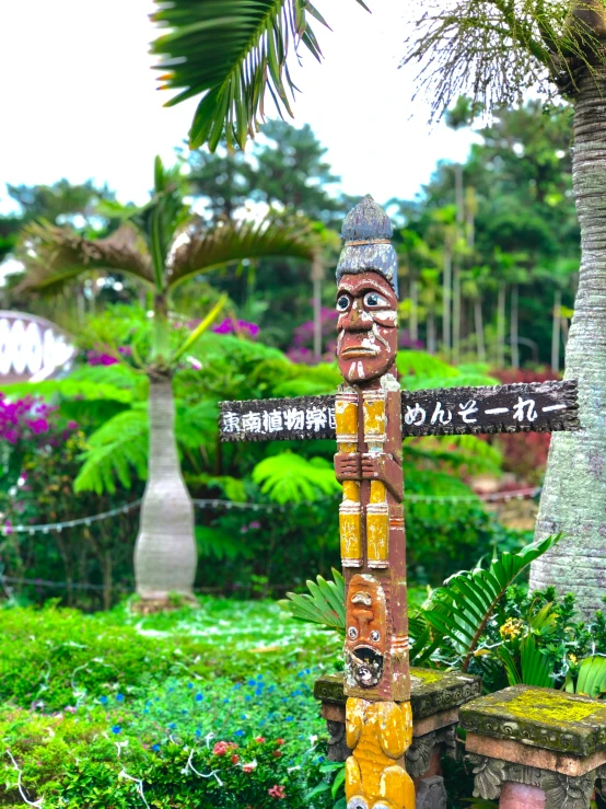 a statue made totem stands in the middle of green bushes