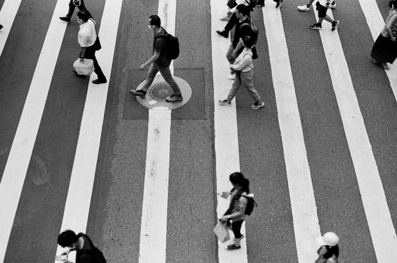 people walking in and out of a crosswalk while one of them is carrying a cell phone