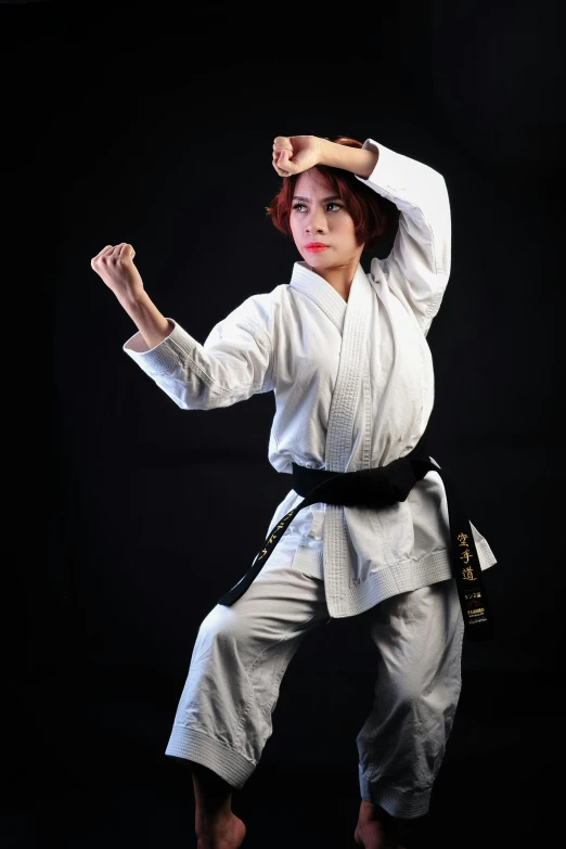 a woman standing in the middle of a black background holding a karate sash