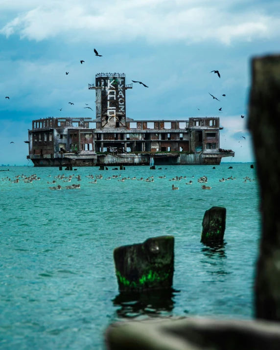 a large building in the ocean with birds flying above