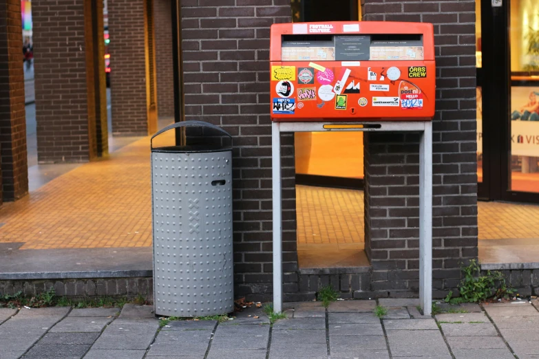 a street side has a newspaper dispenser and trash can