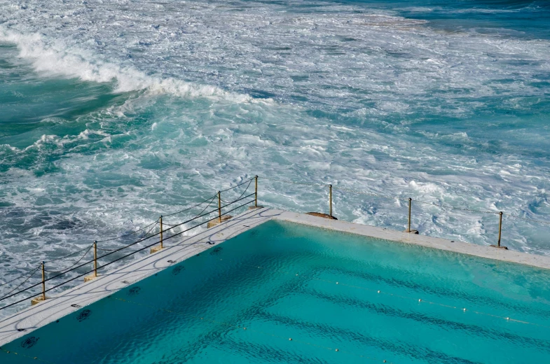 an empty swimming pool on the edge of the sea with waves rolling in