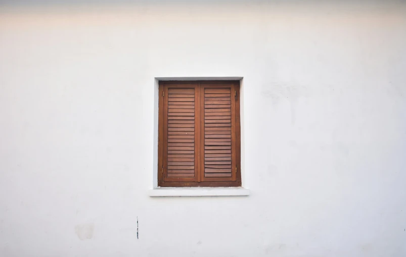 the white wall has a wooden window with shades