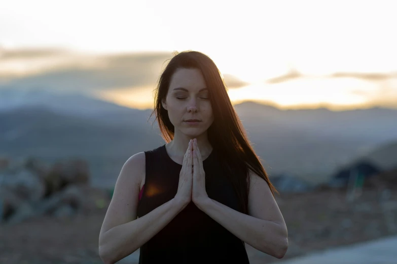 a young woman meditating while standing on top of a hill