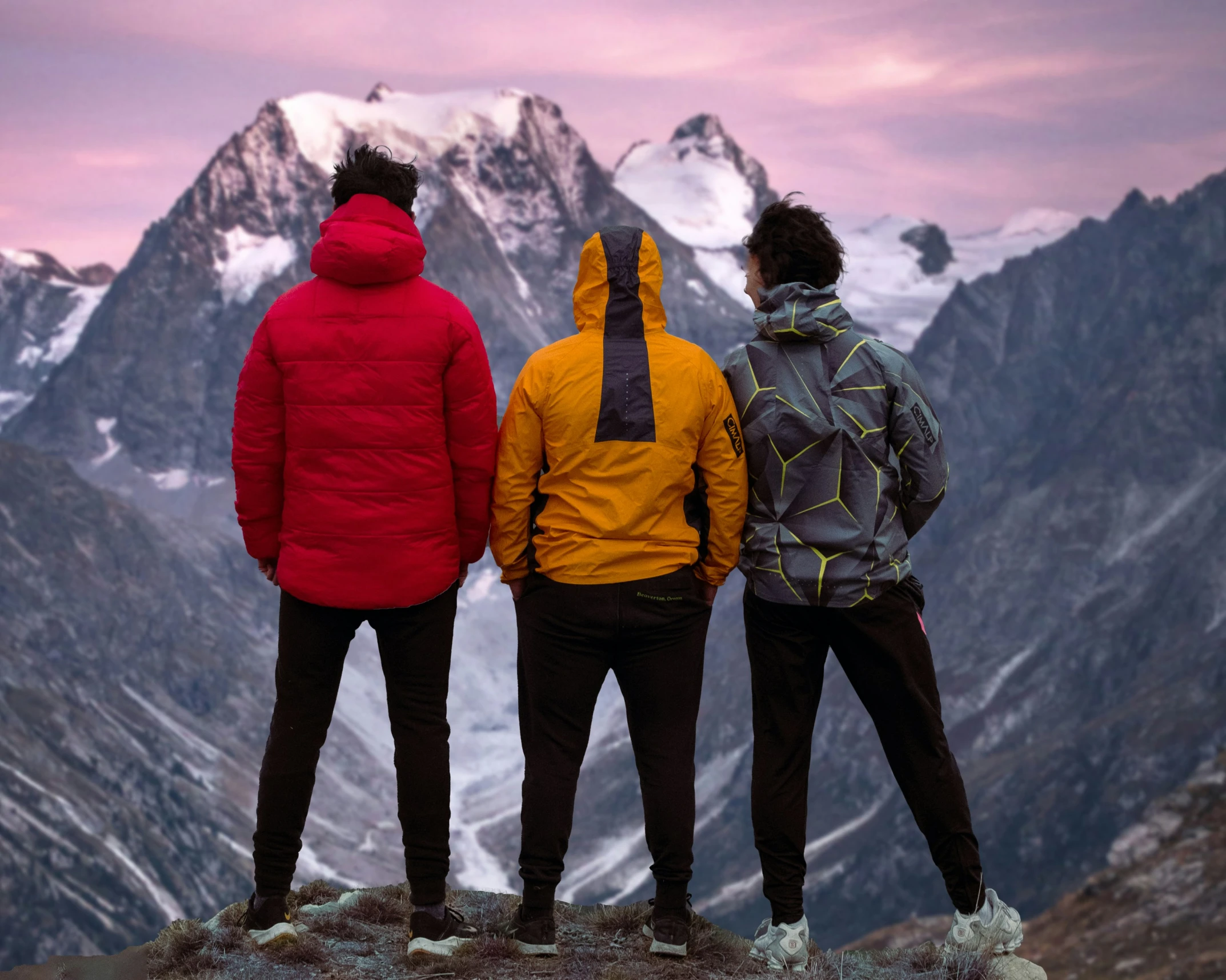 three men stand in the mountains while the sun sets