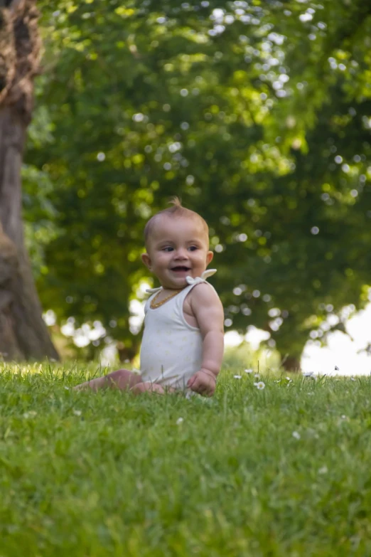 a baby is standing in the grass by a tree