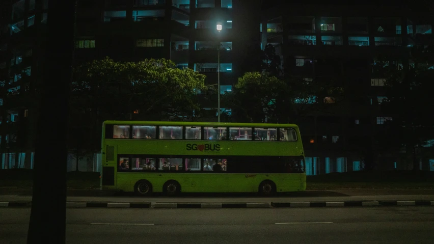 a green double decker bus parked in front of a large building at night