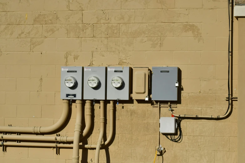three electrical meters attached to a brown brick wall