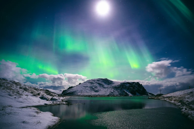 an aurora light over some snowy mountains and a lake