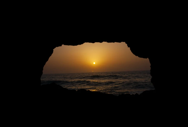 the sun setting through an arch in the cave