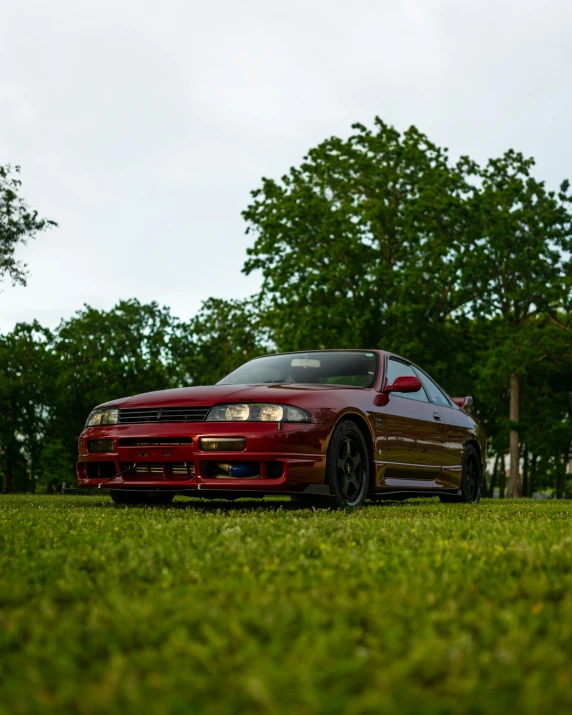 a maroon sports car sits in the grass