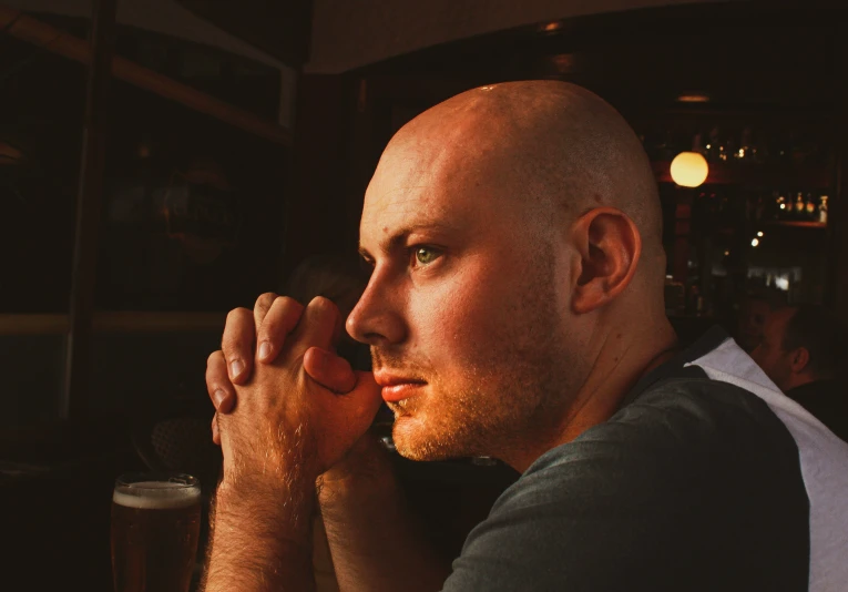 a bald man drinking a pint of beer