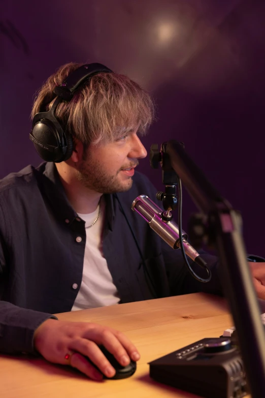 a man wearing headphones sitting in front of a microphone with his laptop on